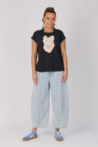 Woman wearing a black t-shirt with a heart design and light blue jeans on a white background
