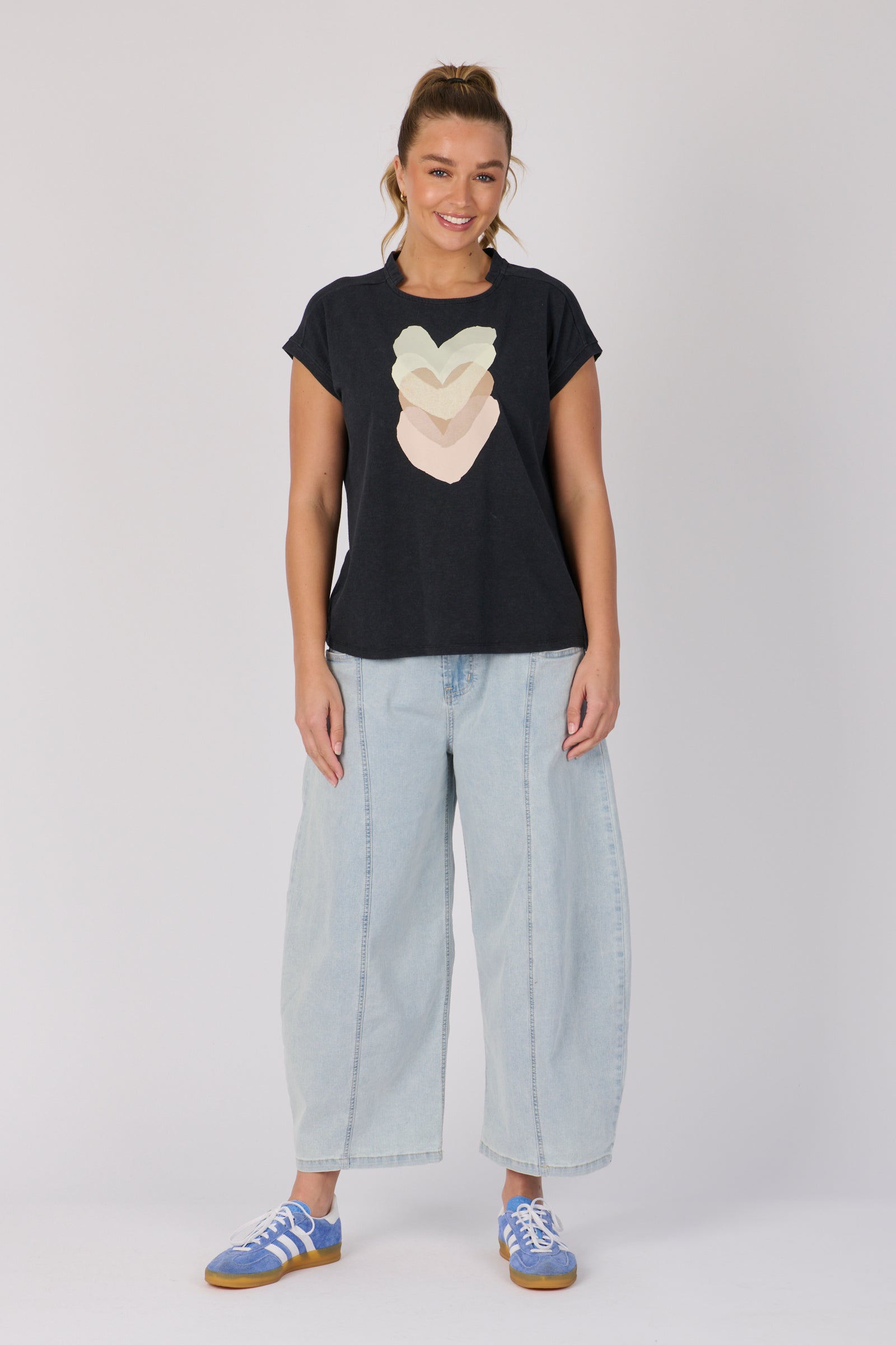 Woman wearing a black t-shirt with a heart design and light blue jeans on a white background