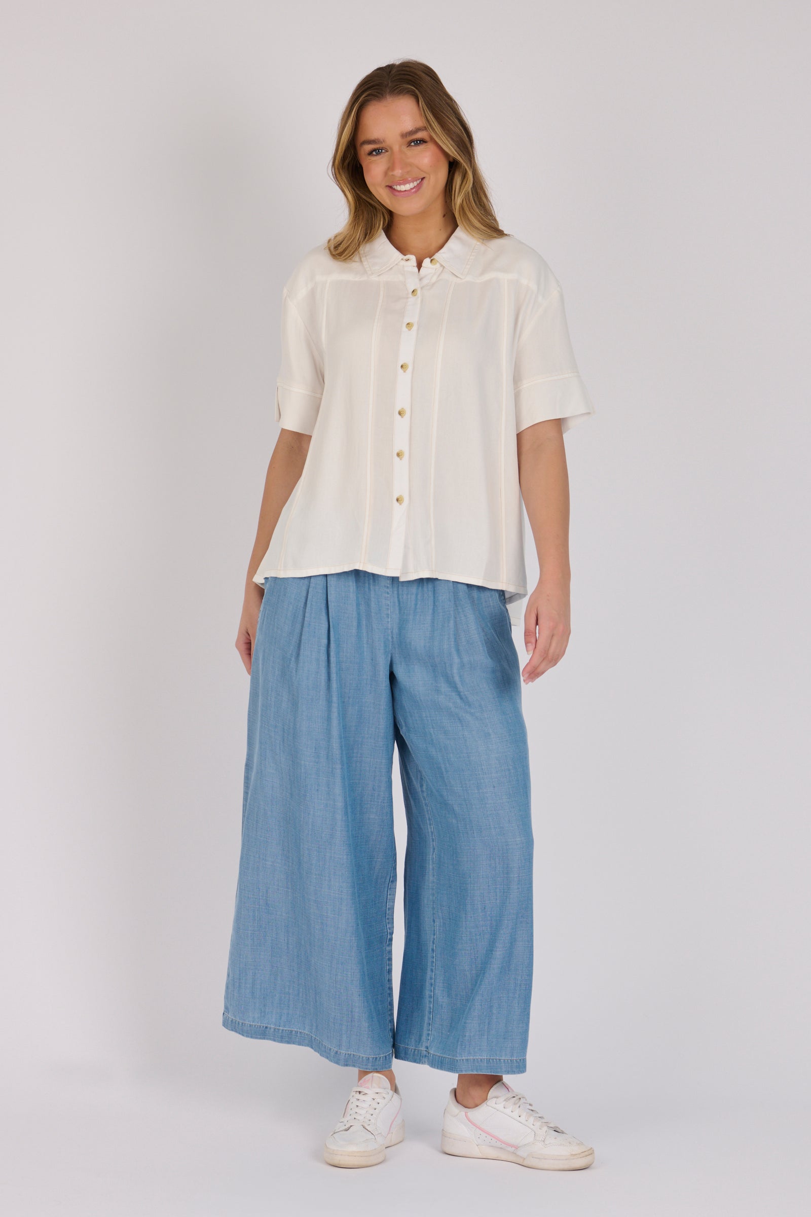 Woman wearing a white 100% lyocell short sleeve button-through shirt with cuffed sleeves and front panel detailing.