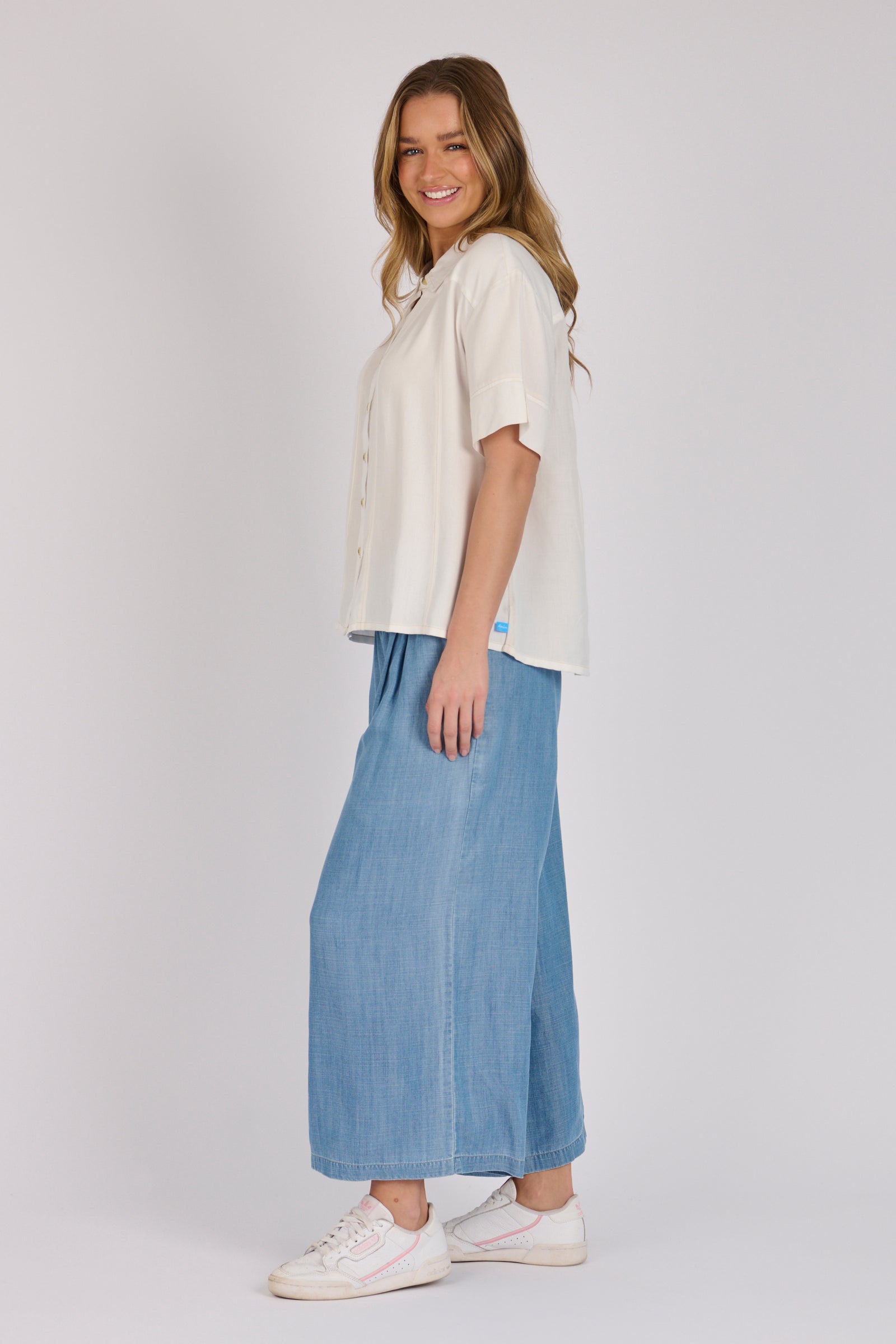 Woman wearing a white 100% lyocell short sleeve button-through shirt with cuffed sleeves and front panel detailing.