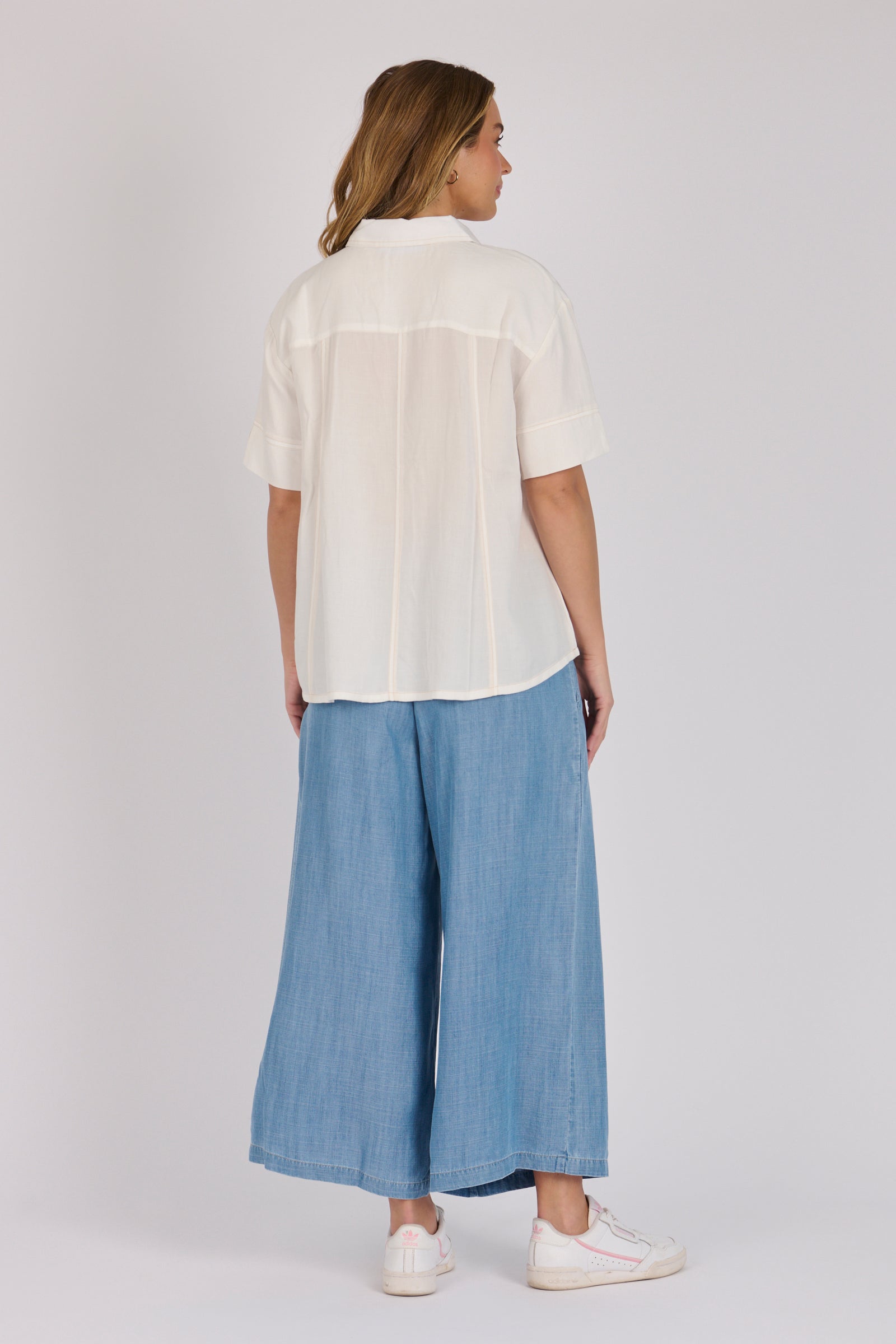 Woman wearing a white 100% lyocell short sleeve button-through shirt with cuffed sleeves and front panel detailing.