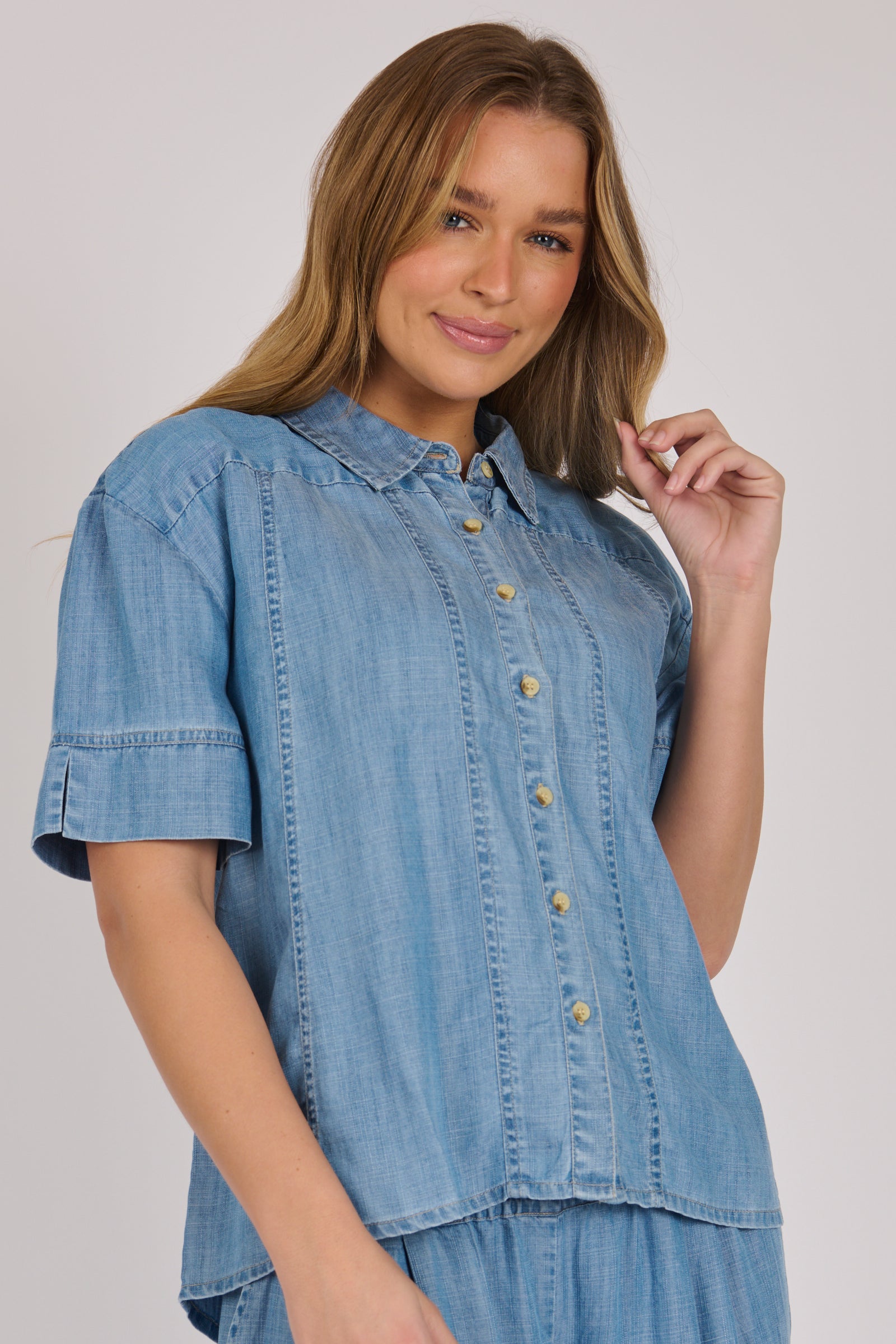 Woman wearing a white 100% lyocell short sleeve button-through shirt with cuffed sleeves and front panel detailing.