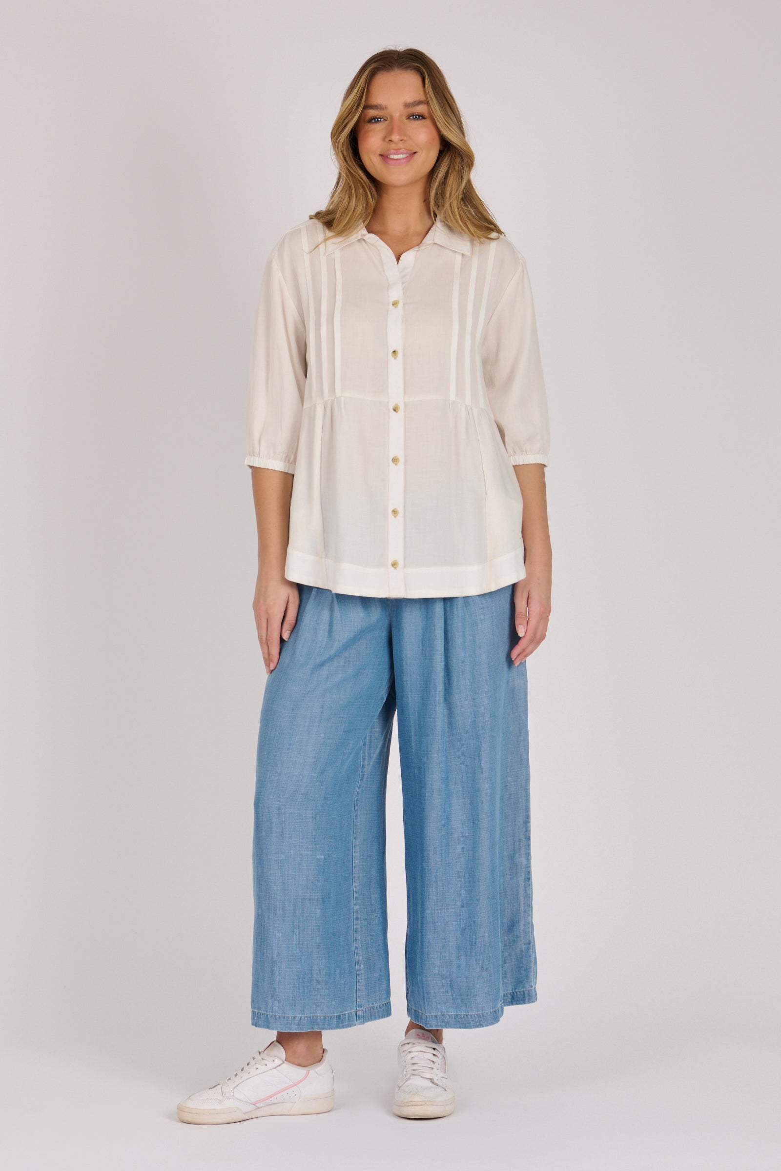 Woman wearing a white 100% lyocell gathered waist blouse with vertical panel detailing, 3/4 elasticated sleeves and a button-through front.