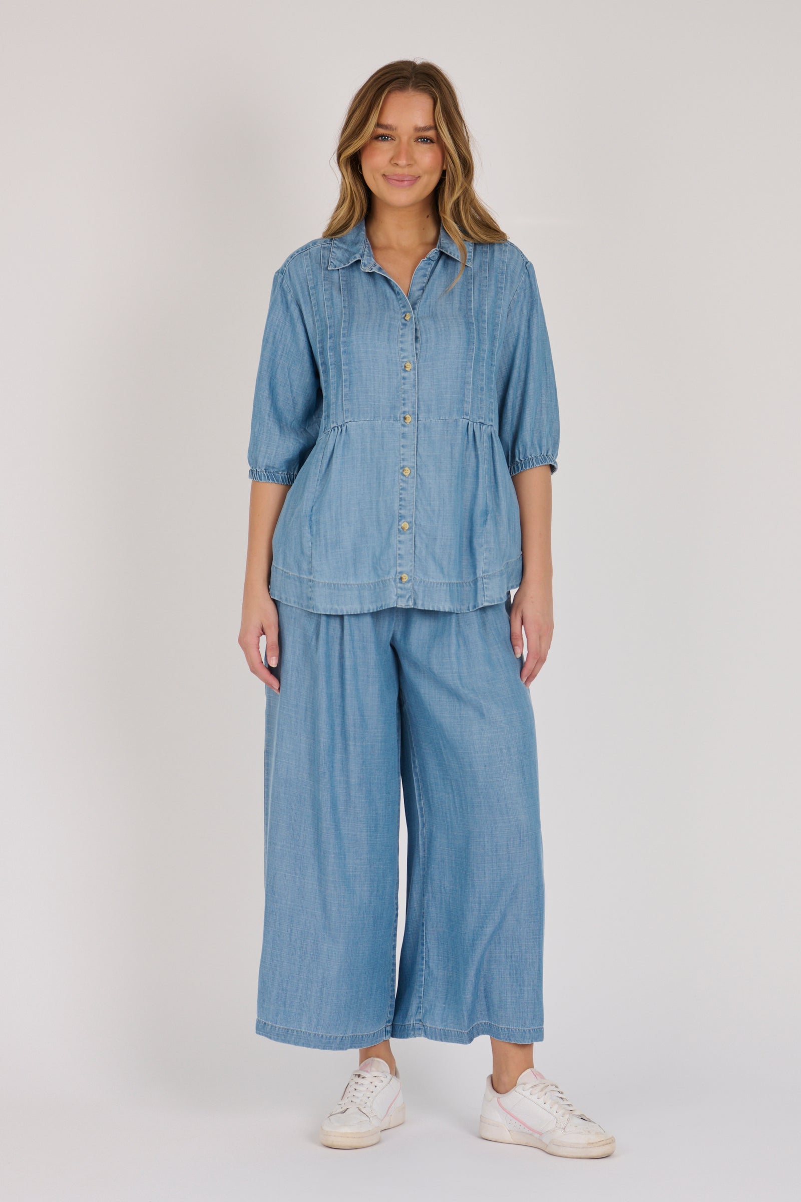 Woman wearing a light blue 100% lyocell gathered waist blouse with vertical panel detailing, 3/4 elasticated sleeves and a button-through front.