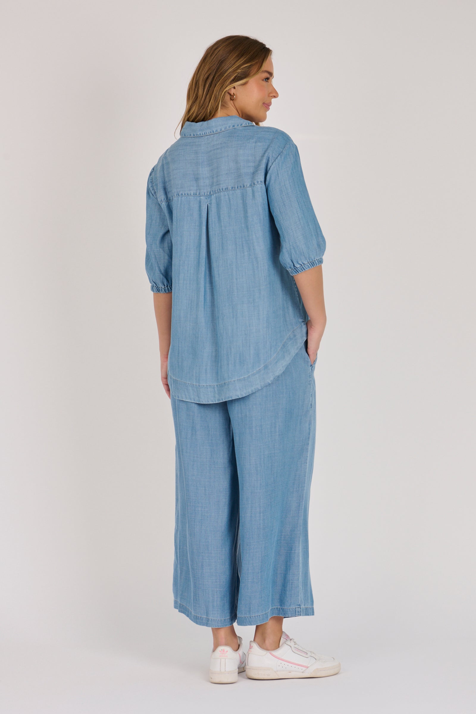 Woman wearing a light blue 100% lyocell gathered waist blouse with vertical panel detailing, 3/4 elasticated sleeves and a button-through front.