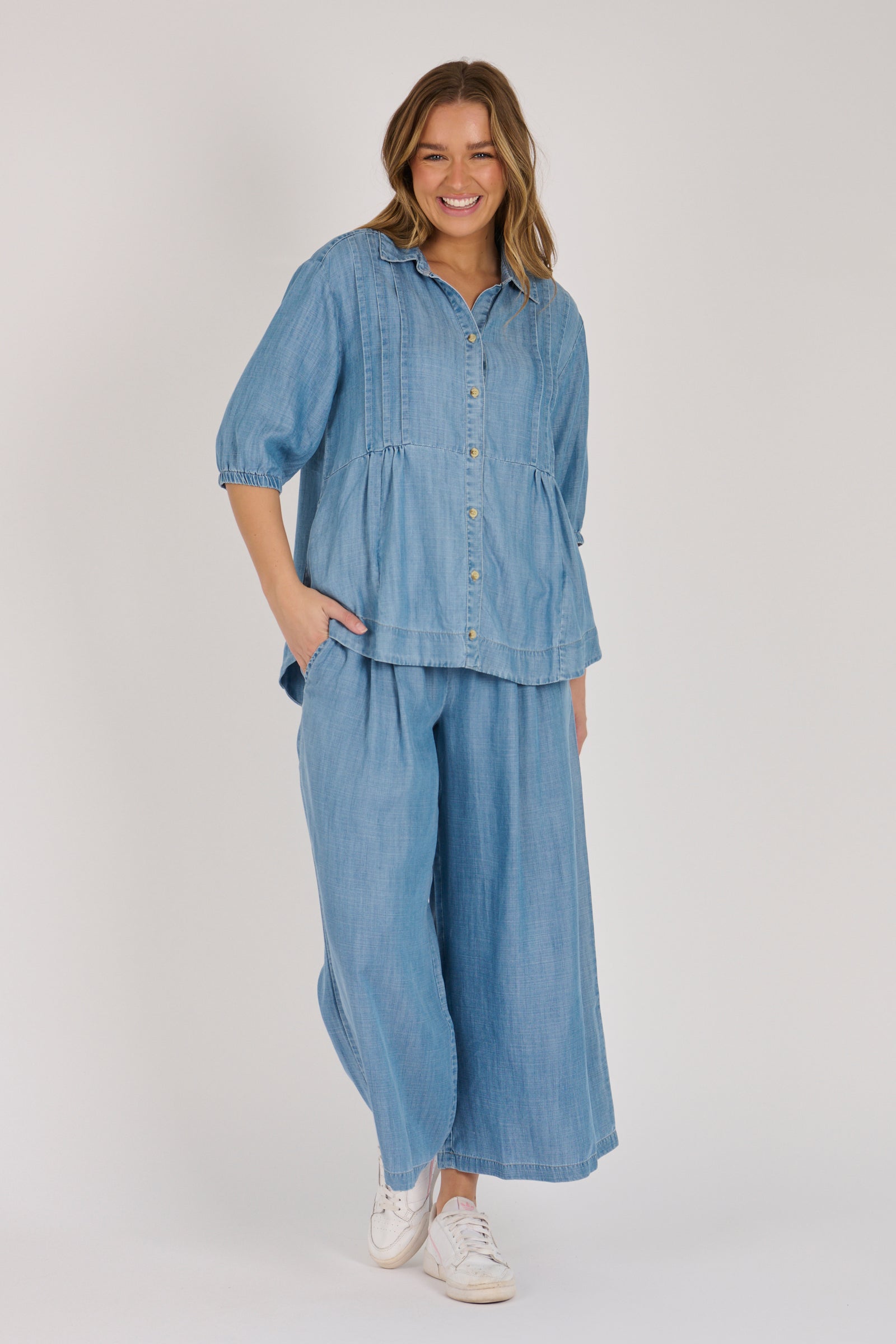 Woman wearing a light blue 100% lyocell gathered waist blouse with vertical panel detailing, 3/4 elasticated sleeves and a button-through front.