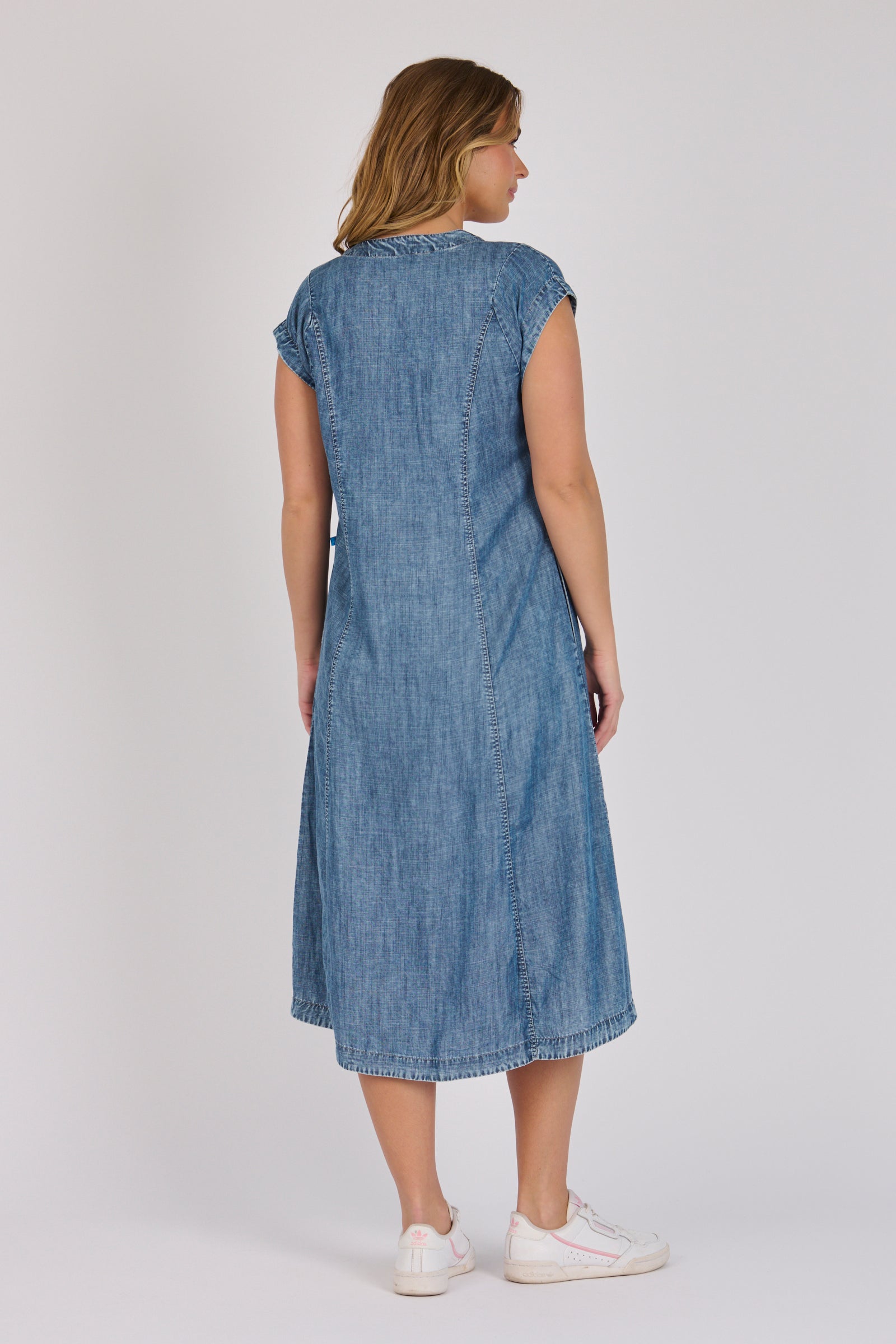 Woman wearing a dark blue 100% lyocell button-through midi dress with panelled seams and cap sleeves.