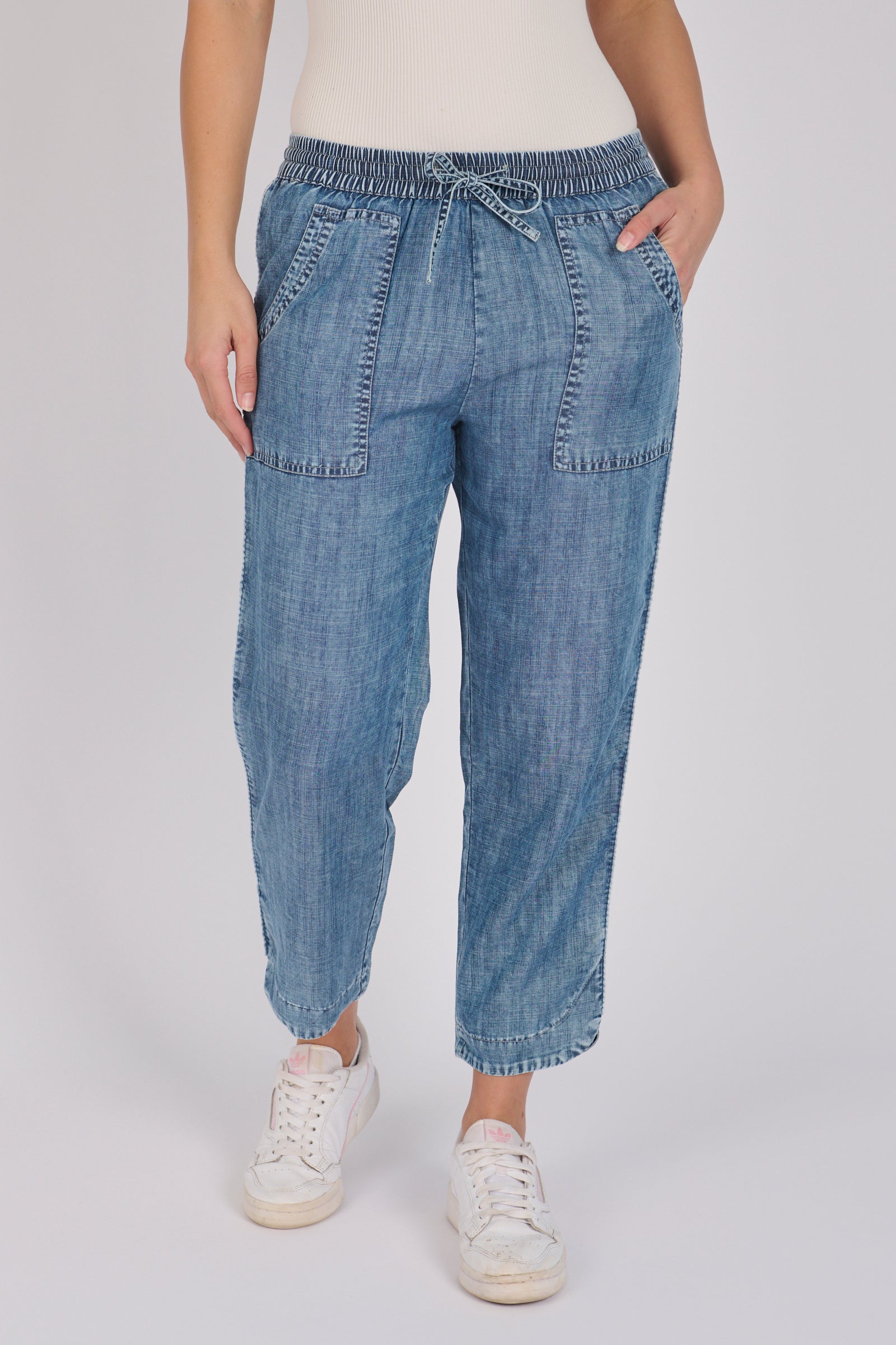 Woman wearing dark blue 100% lyocell beach pants with contrast piping, patch pockets and a relaxed tapered leg.