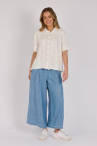 Woman wearing a white 100% lyocell short sleeve button-through shirt with cuffed sleeves and front panel detailing.
