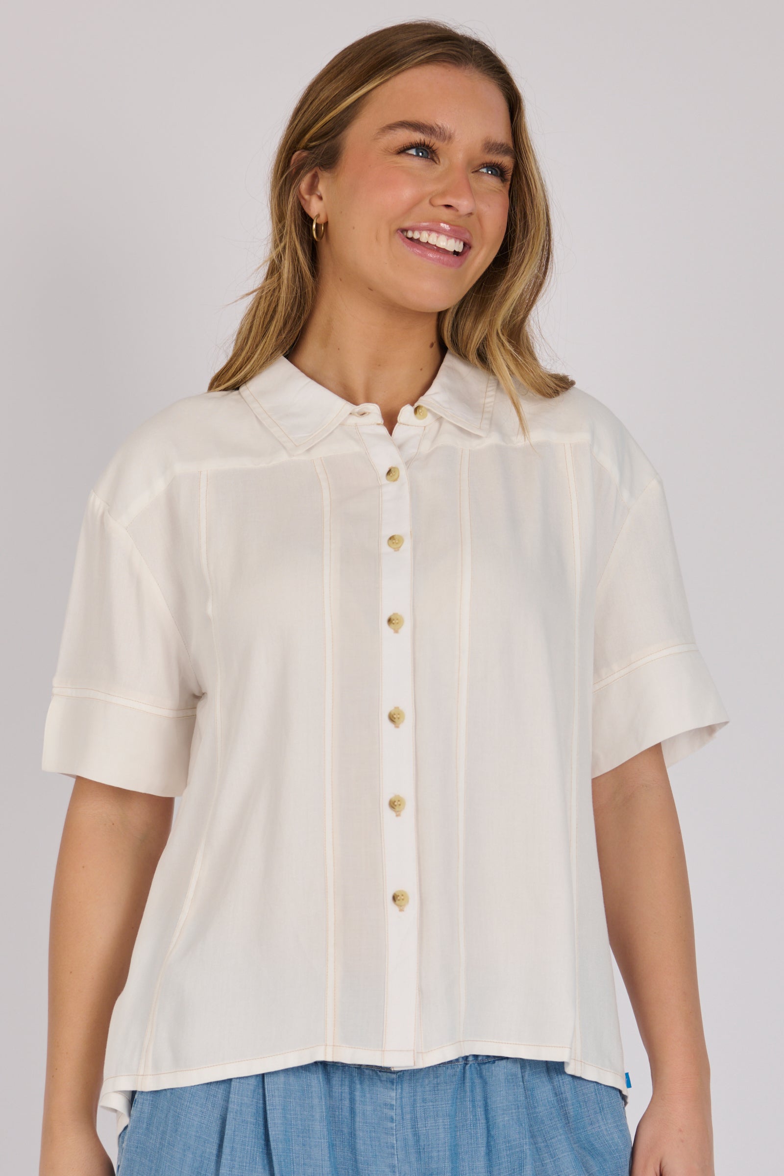 Woman wearing a white 100% lyocell short sleeve button-through shirt with cuffed sleeves and front panel detailing.
