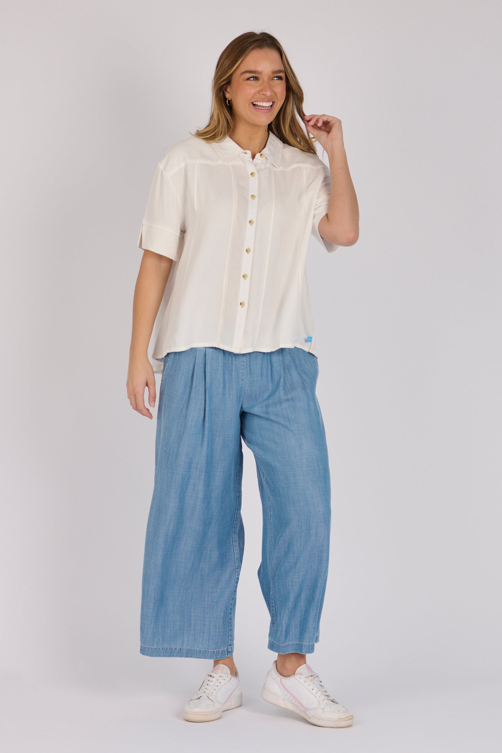 Woman wearing a white 100% lyocell short sleeve button-through shirt with cuffed sleeves and front panel detailing.
