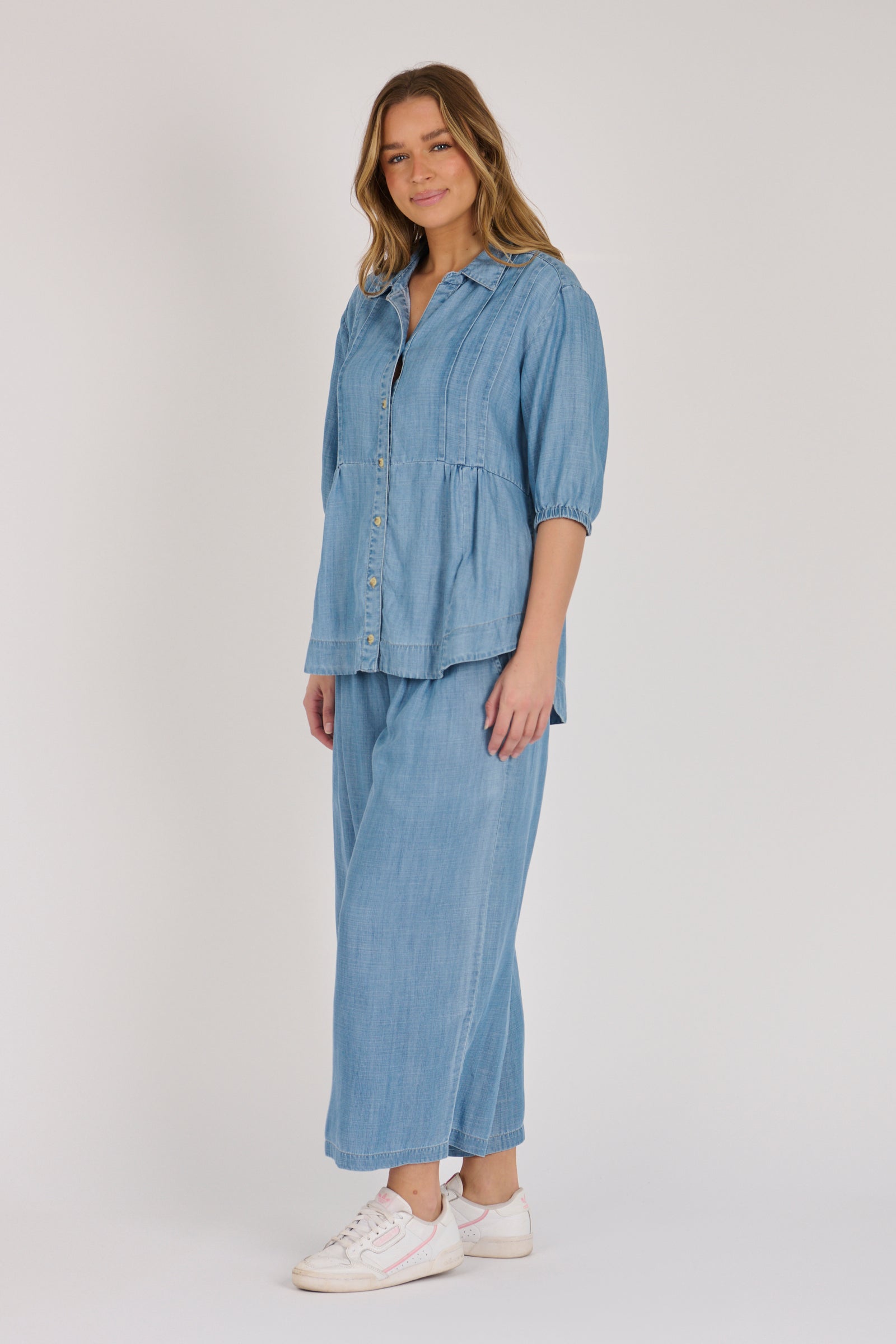 Woman wearing a light blue 100% lyocell gathered waist blouse with vertical panel detailing, 3/4 elasticated sleeves and a button-through front.