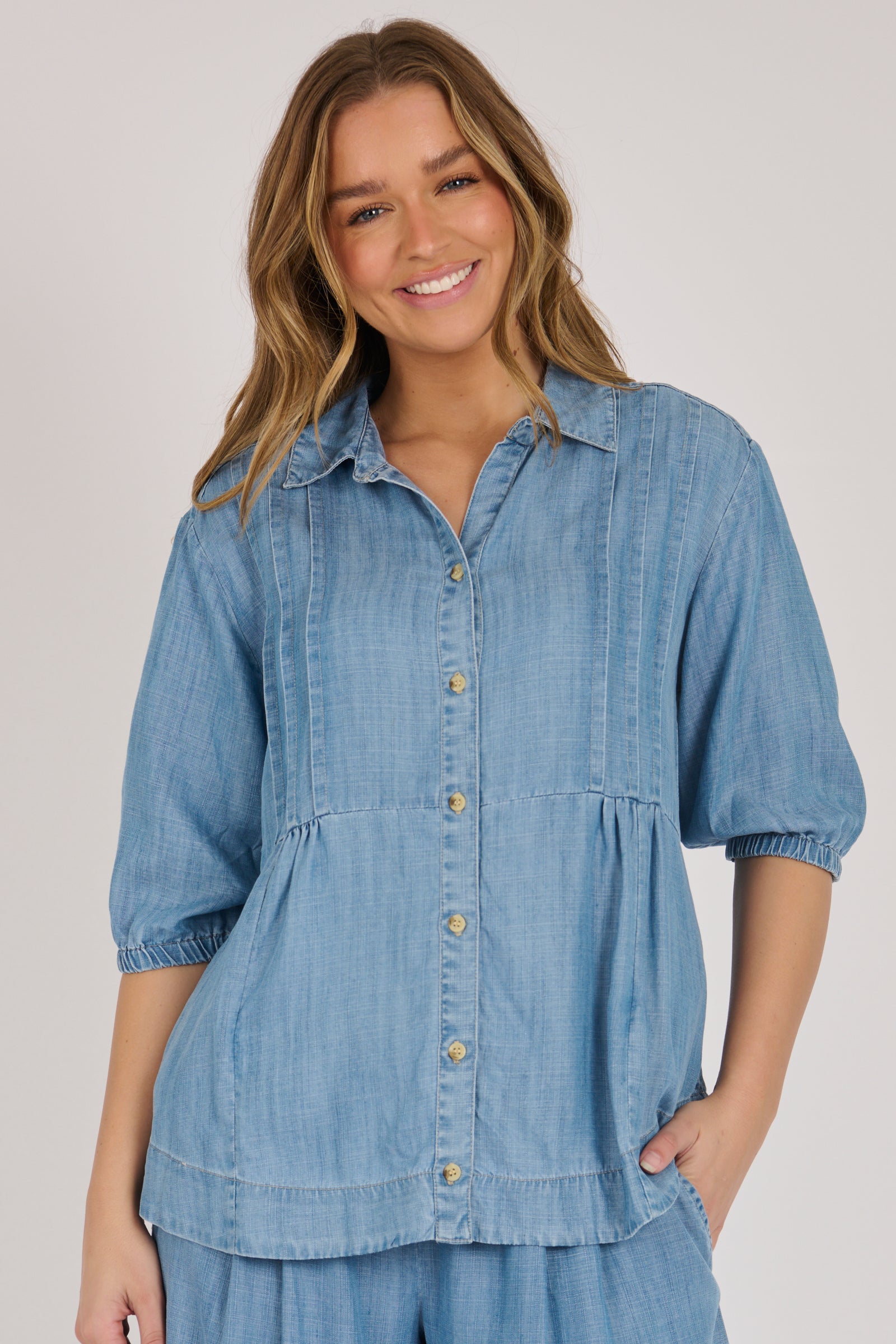 Woman wearing a light blue 100% lyocell gathered waist blouse with vertical panel detailing, 3/4 elasticated sleeves and a button-through front.