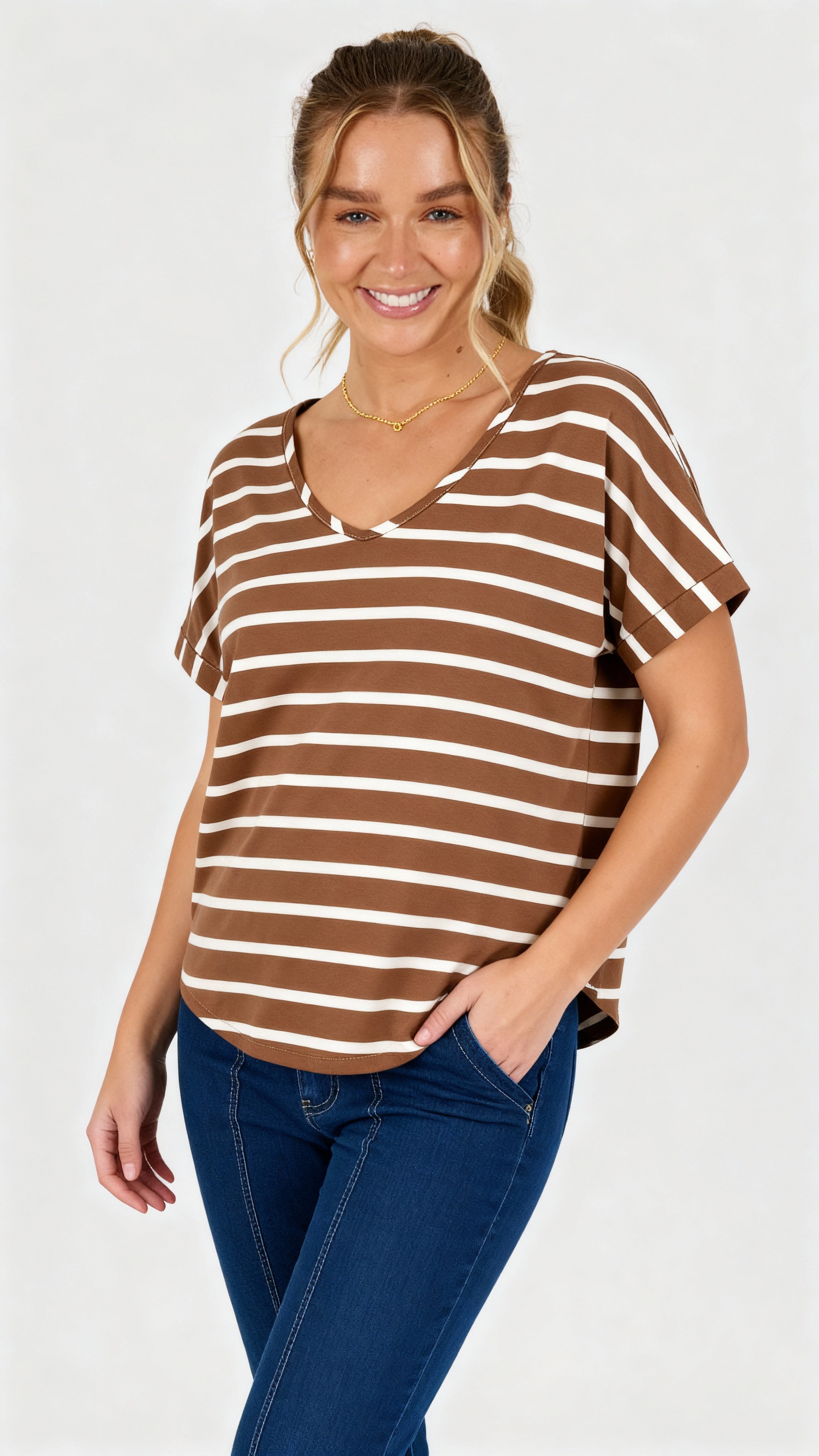 Woman wearing a acorn and white striped v-neck curve hem tee with blue jeans on a white background